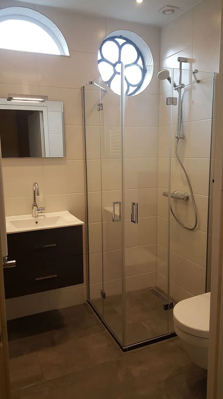 Douchecabine met glazen vouwdeuren onder het ronde raam — badkamerrenovatie in Oosterpoort door BontBouw