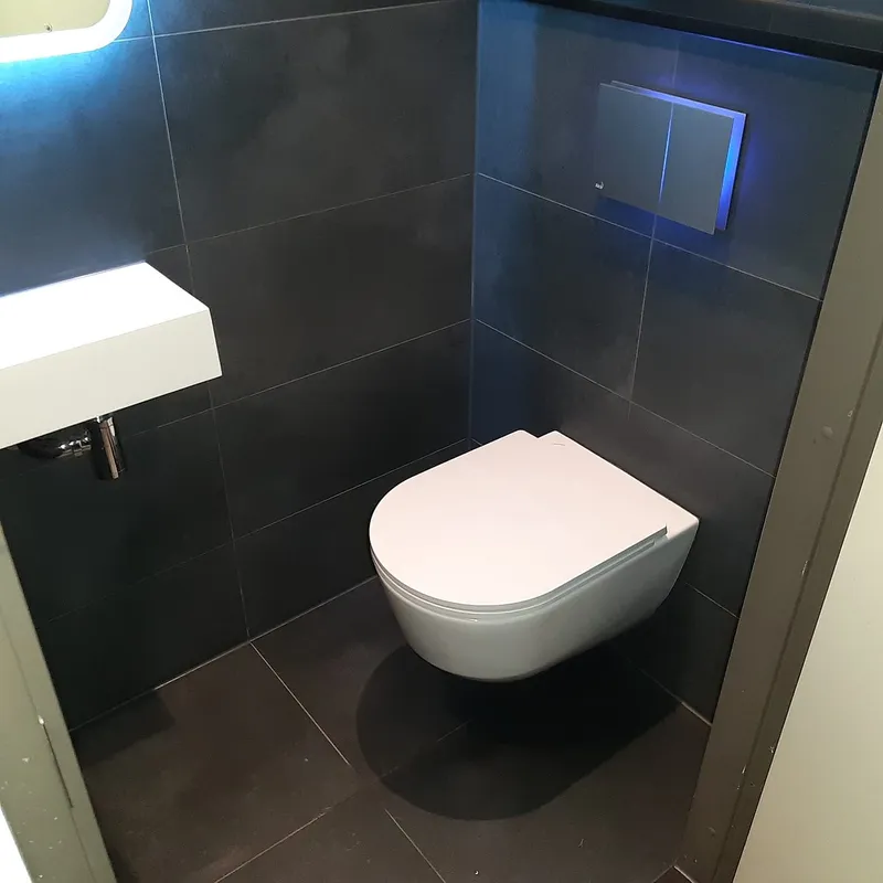 Hangtoilet met blauw verlichte bedieningsplaat op antracieten tegels — toiletrenovatie in Beijum door BontBouw