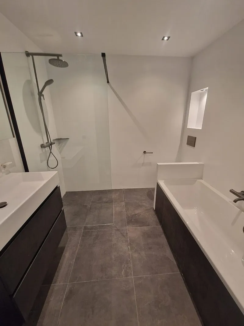 Inloopdouche met glazen wand en ligbad met antracieten front — badkamerrenovatie in Roden door BontBouw