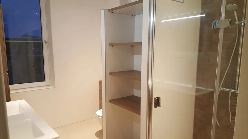 Open kast met houten schappen naast de douchecabine — badkamerrenovatie in Hoogezand door BontBouw