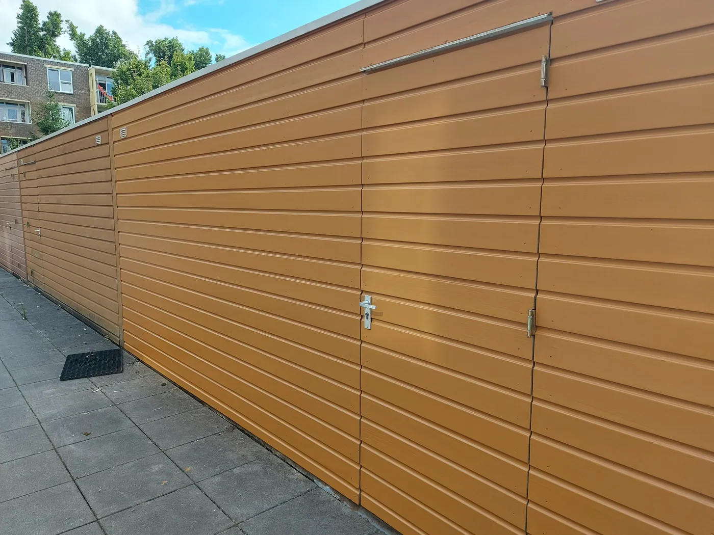 Rij houten bergingen met nieuwe laag langs het pad na het werk — schilderwerk in Groningen door BontBouw