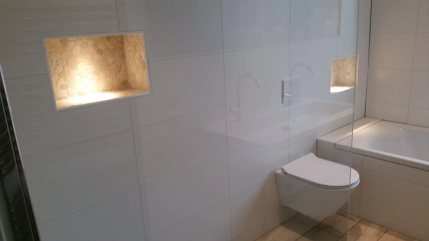 Verlichte nis met kiezeltegels en hangtoilet bij het ligbad na de renovatie — badkamerrenovatie in Haren door BontBouw