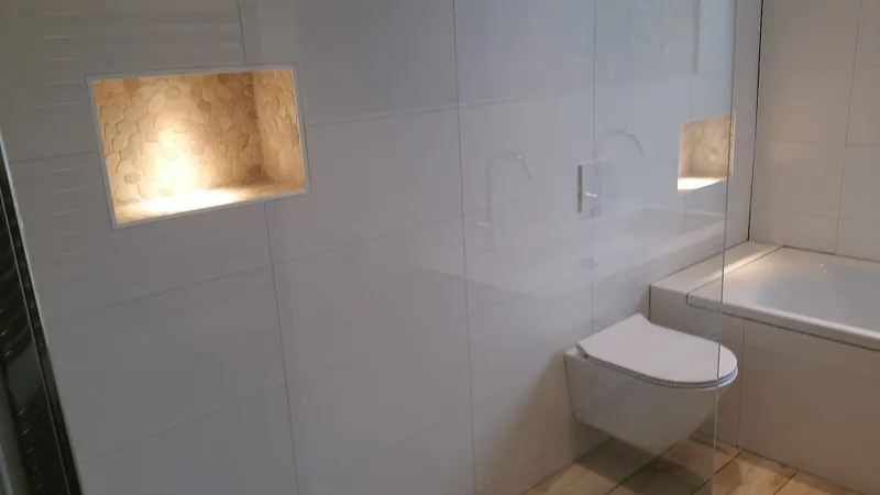 Verlichte nis met kiezeltegels en hangtoilet bij het ligbad — badkamerrenovatie in Haren door BontBouw