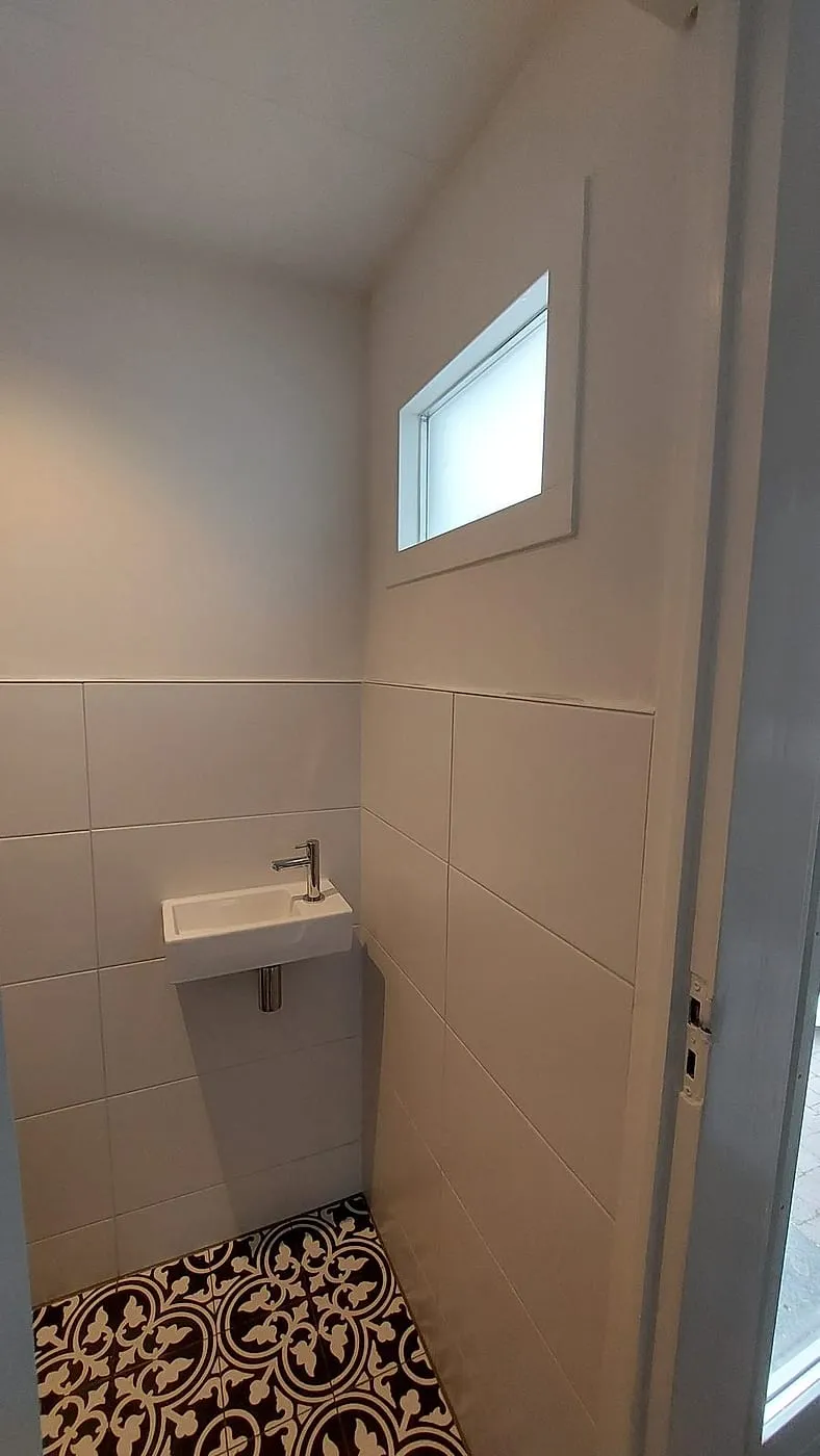 Fontein onder het hoge raampje met lichte wandtegels — toiletrenovatie in Korrewegwijk door BontBouw