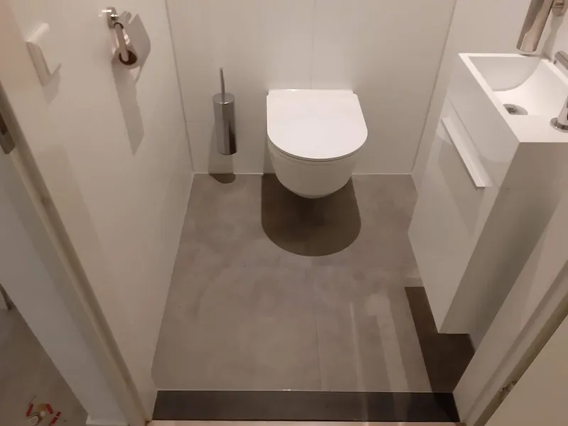 Grijze vloertegels met hangtoilet en wit fonteinkastje — toiletrenovatie in Herewegbuurt door BontBouw