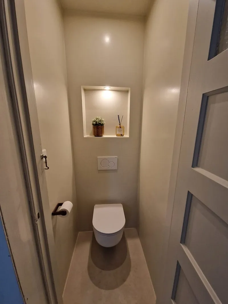 Hangtoilet met verlichte nis en gietvloer in warm beige — toiletrenovatie in Korrewegwijk door BontBouw