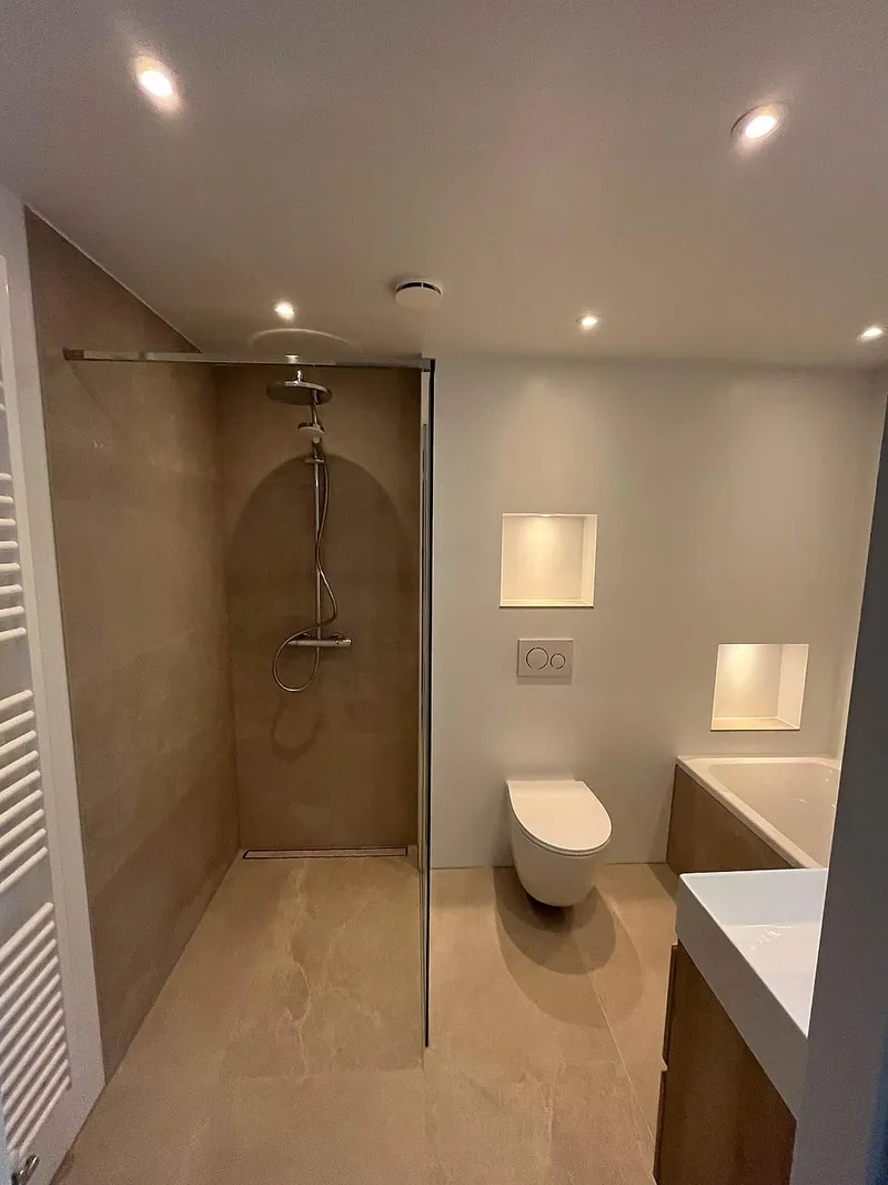 Inloopdouche met beige tegels en verlichte nissen bij het hangtoilet — badkamerrenovatie in Beijum door BontBouw