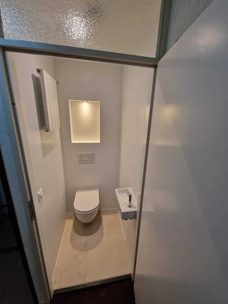 Toiletruimte met glaswand en verlichte nis boven het hangtoilet — toiletrenovatie in Ulgersmaborg door BontBouw