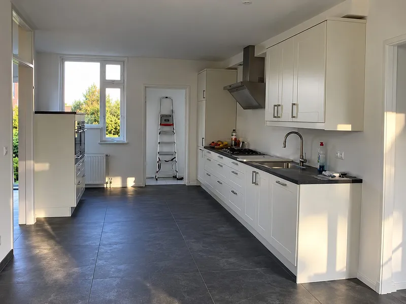 Witte keuken met kaderdeuren langs lange wand en donkere tegelvloer — keukenrenovatie in Groningen door Bontbouw