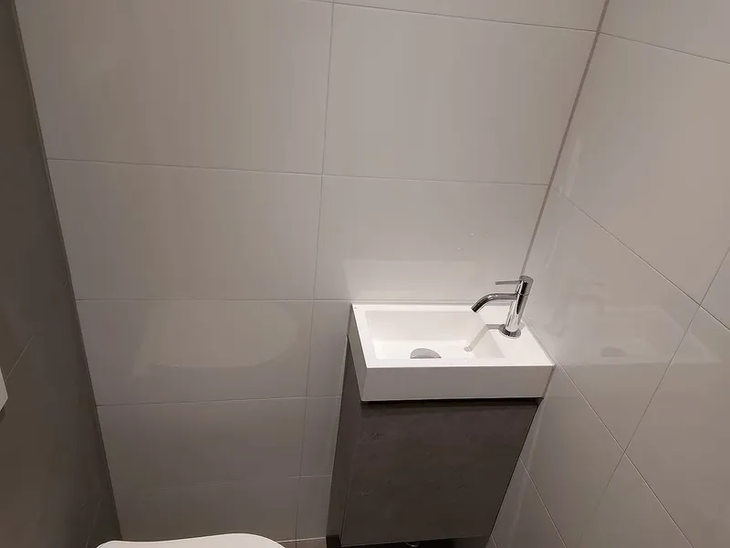 Fontein met chromen kraan op een kastje in betonlook — toiletrenovatie in Schildersbuurt door BontBouw