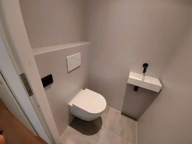 Hangtoilet met witte bedieningsplaat en lichte vloertegels — toiletrenovatie in Korrewegwijk door BontBouw