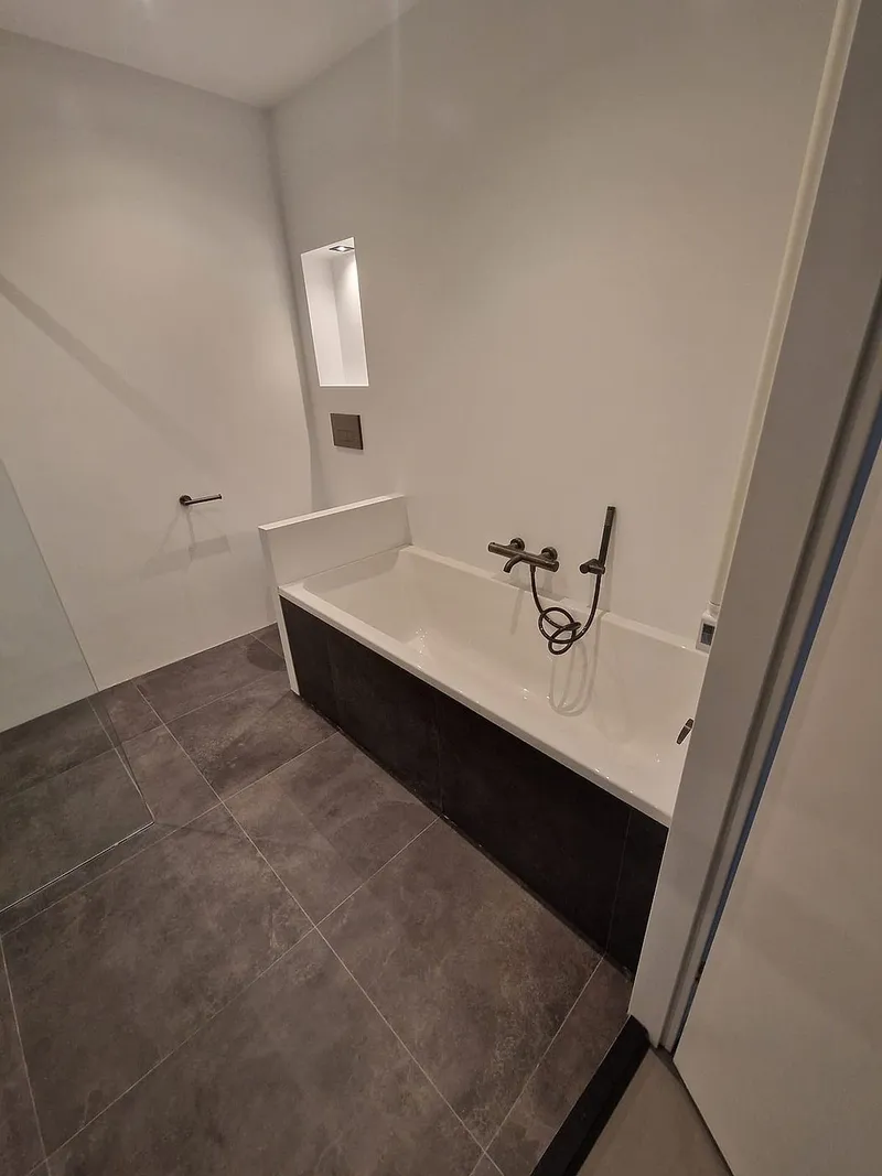 Ligbad met antracieten front en verlichte nis in de schuine wand — badkamerrenovatie in Roden door BontBouw
