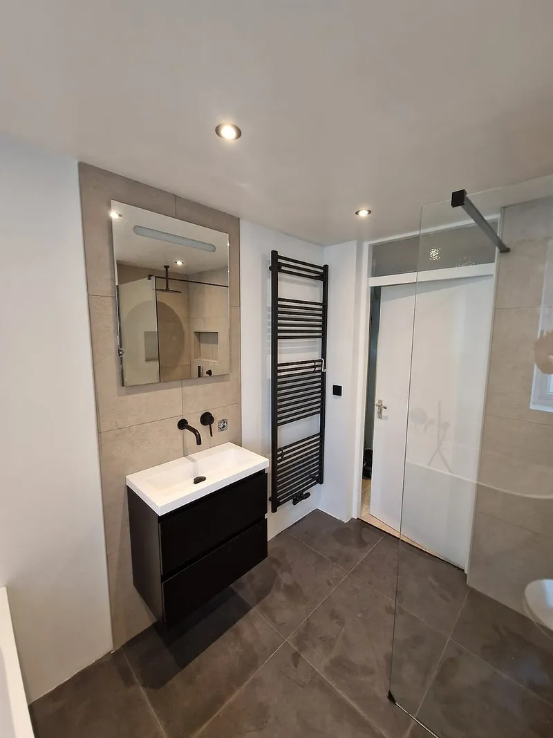 Wastafel met spiegelkast en zwarte radiator — badkamerrenovatie in Ulgersmaborg door BontBouw