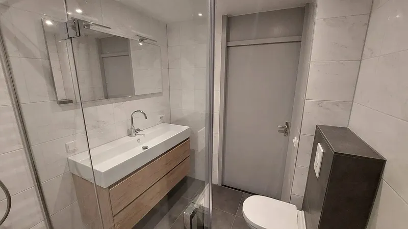 Wastafelmeubel met spiegel en hangtoilet naast de douchecabine — badkamerrenovatie in De Hunze door BontBouw