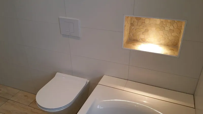 Witte bedieningsplaat en verlichte kiezelnis bij het ligbad — badkamerrenovatie in Haren door BontBouw