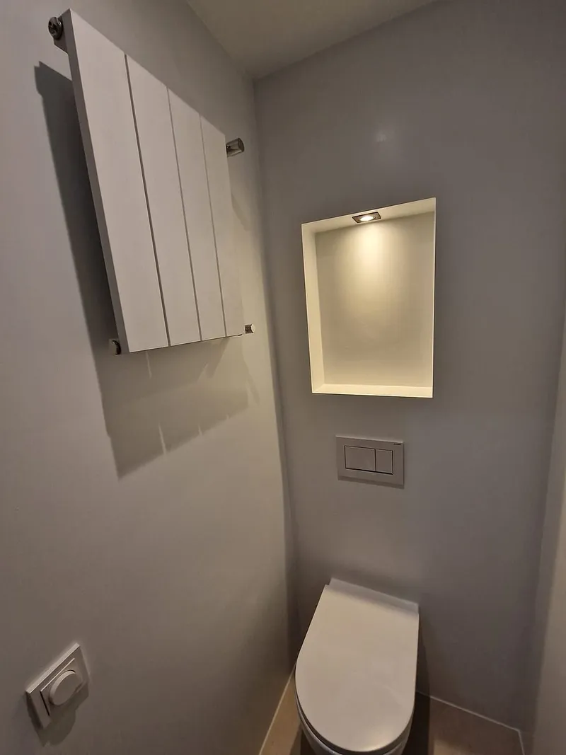 Witte designradiator naast de verlichte nis — toiletrenovatie in Ulgersmaborg door BontBouw