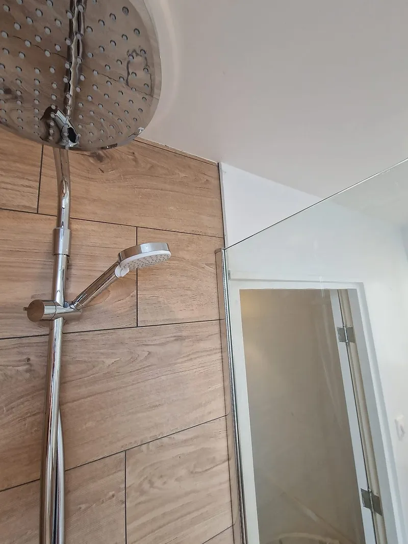 Chromen regendouche met handdouche tegen houtlook tegels — badkamerrenovatie in Leeuwarden door BontBouw