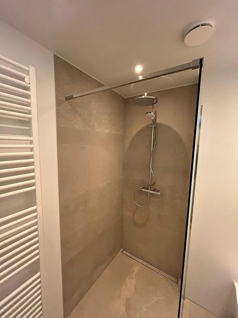 Regendouche met douchegoot tegen beige wandtegels — badkamerrenovatie in Beijum door BontBouw