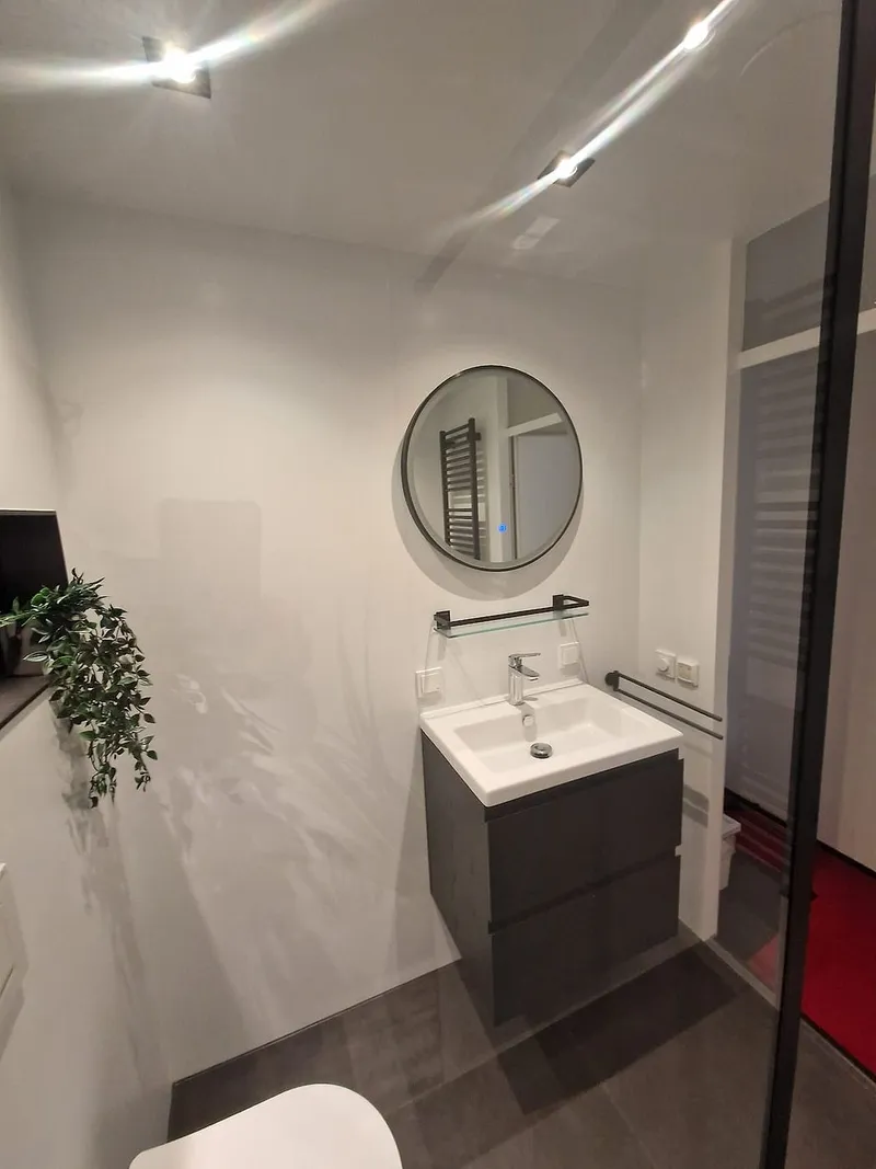 Ronde spiegel boven antracieten wastafelmeubel met glazen planchet — badkamerrenovatie in De Hunze door BontBouw