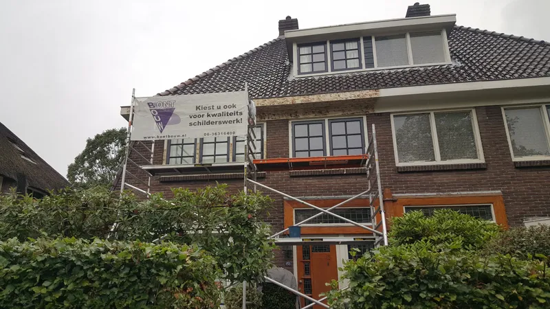 Voorgevel met rolsteiger spandoek en geschuurde overstek — schilderwerk in Assen door BontBouw