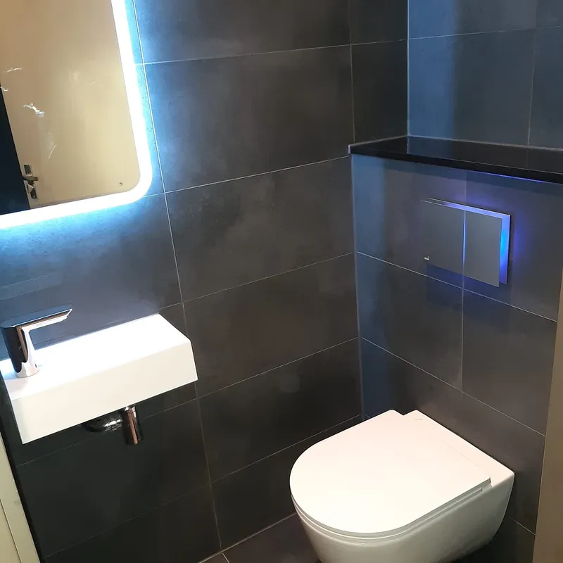 Hangtoilet met zwart blad en blauw verlichte bedieningsplaat — toiletrenovatie in Beijum door BontBouw