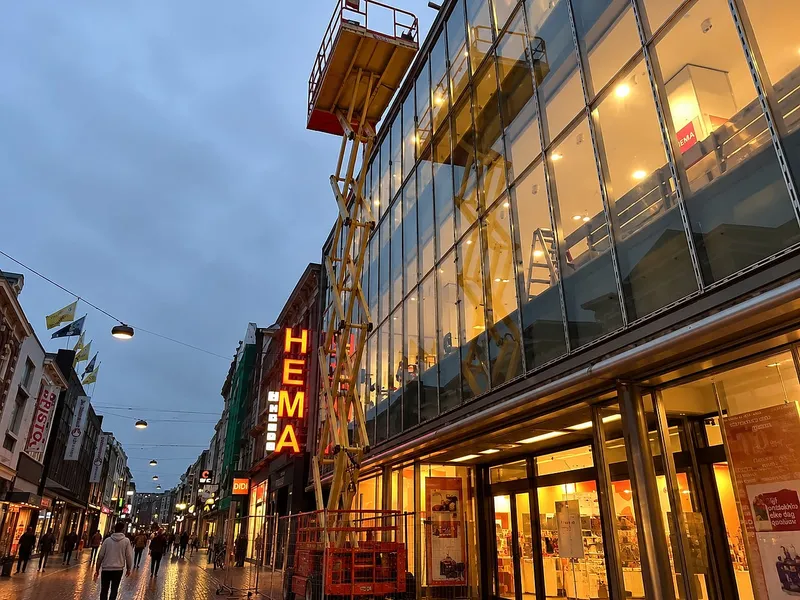 Uitgeschoven hoogwerker langs glazen gevel in winkelstraat — plaatsen & aanleggen in Groningen door BontBouw