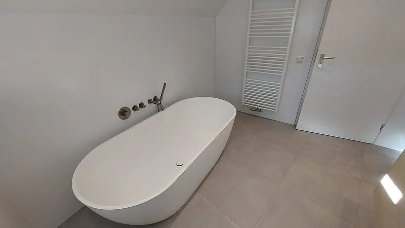 Vrijstaand bad met witte handdoekradiator en grote vloertegels — badkamerrenovatie in Eelderwolde door BontBouw