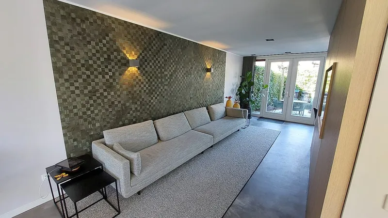 Woonkamer met mozaiekwand en lange bank — complete verbouwing in Eelderwolde door BontBouw