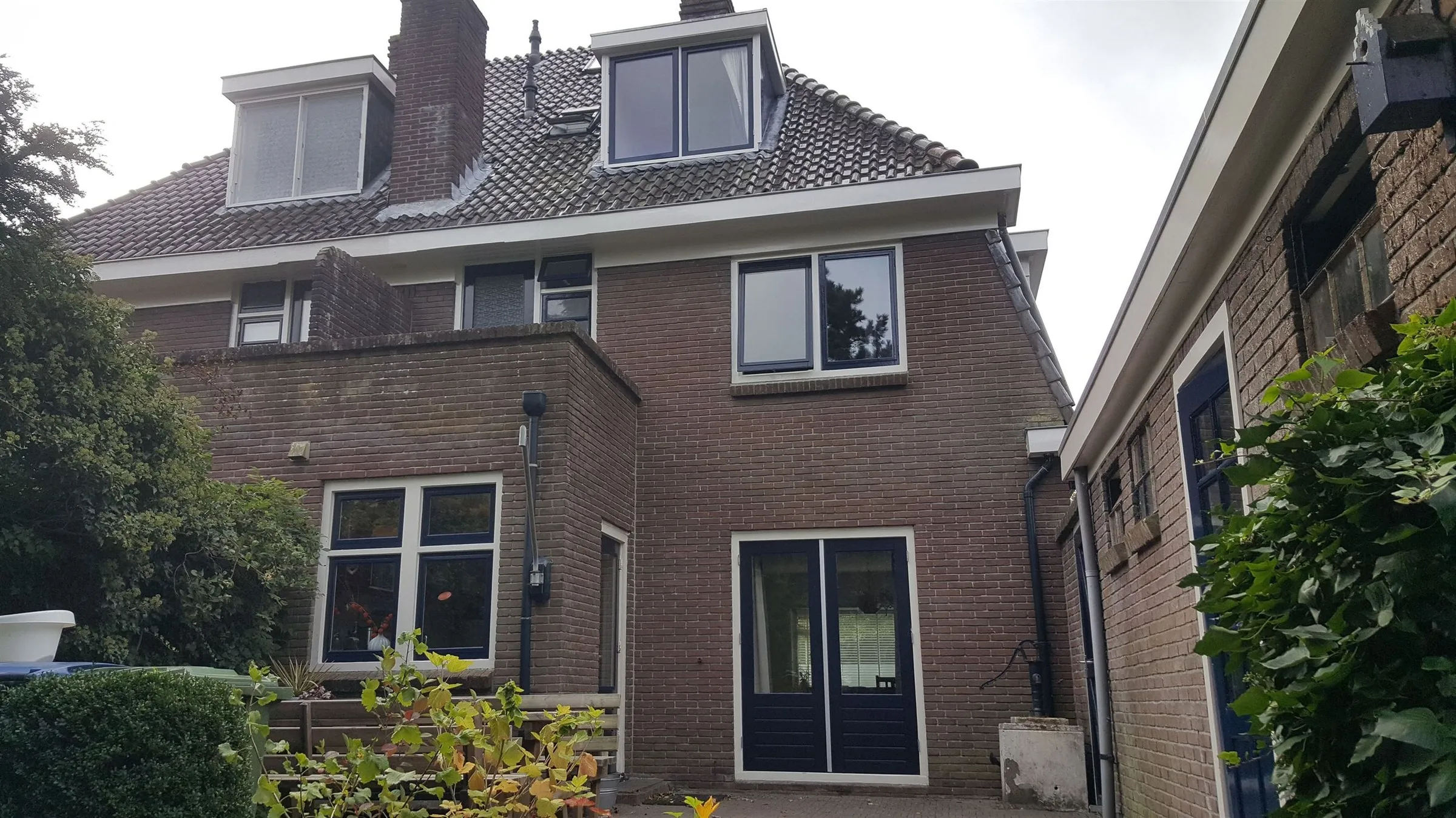 Achtergevel met donkerblauwe deuren en creme kozijnen na het werk — schilderwerk in Assen door BontBouw