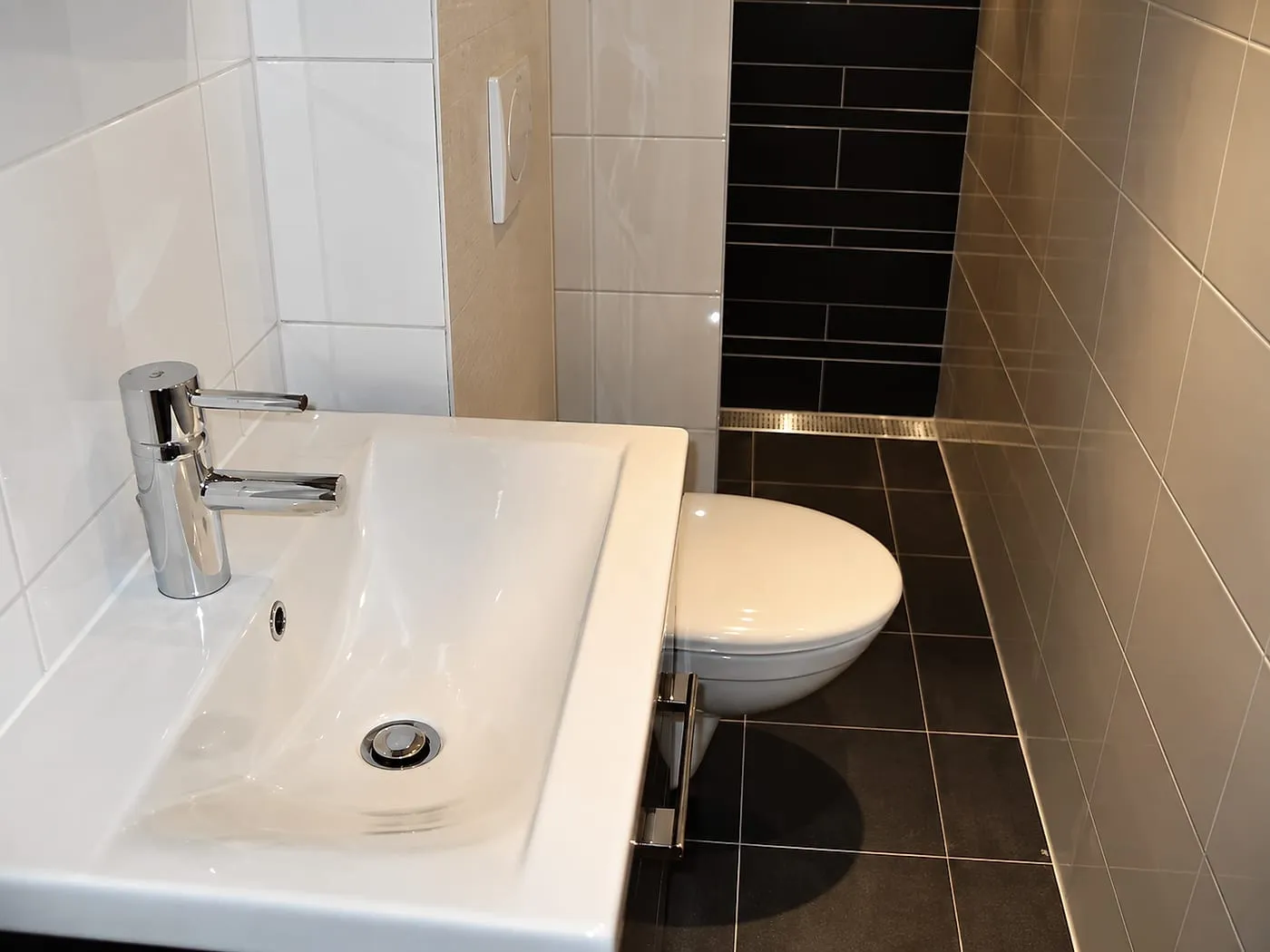 Brede witte wastafel en hangtoilet bij donkere achterwand na de renovatie — badkamerrenovatie in Groningen door BontBouw