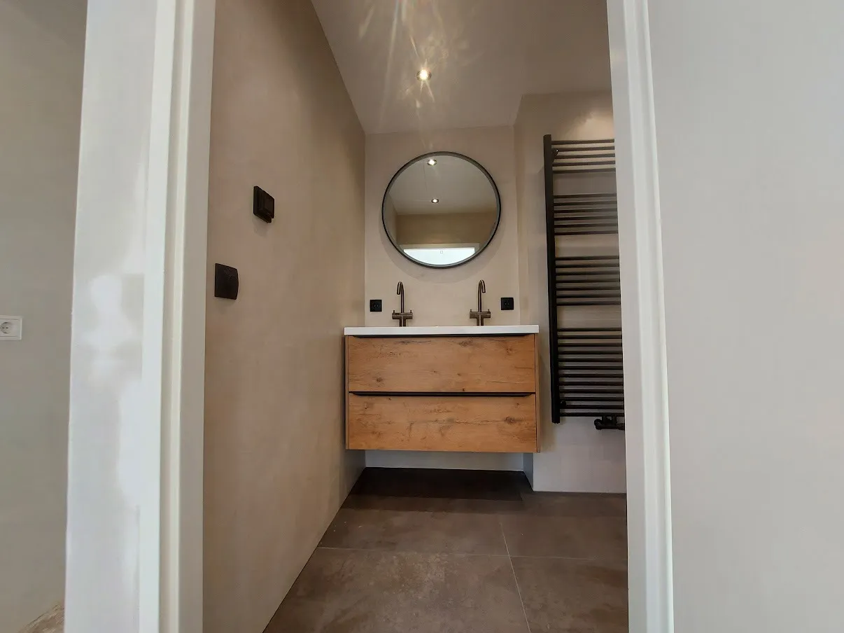 Doorkijk naar het eiken meubel met ronde spiegel na de renovatie — badkamerrenovatie in Groningen door BontBouw