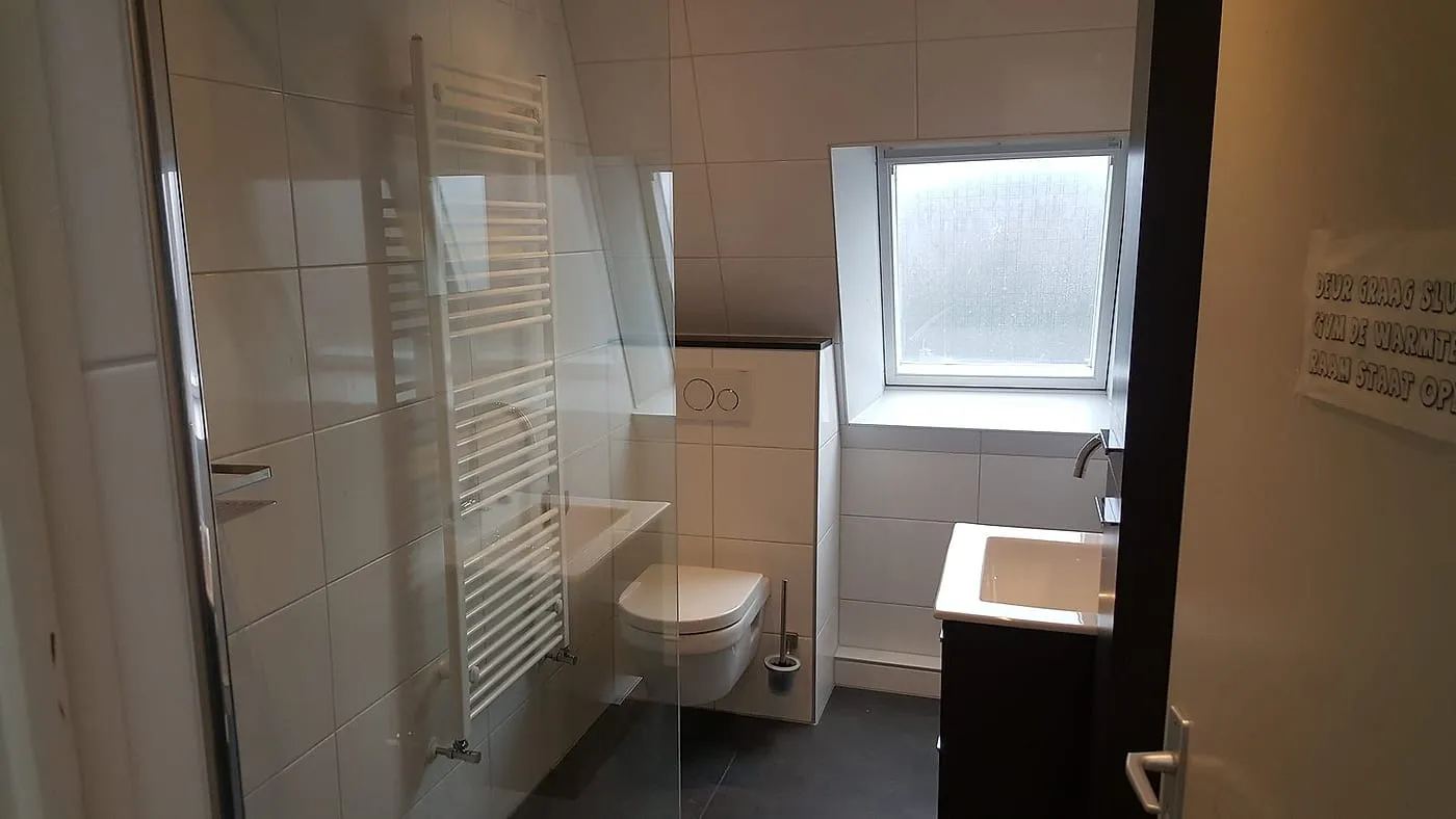 Hangtoilet met witte handdoekradiator en donkere wastafelkast na de renovatie — badkamerrenovatie in De Hoogte door BontBouw