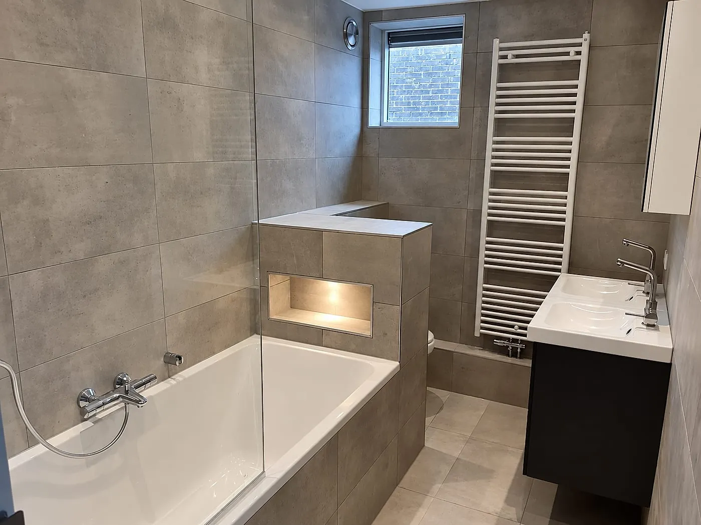 Ligbad met dubbele wastafel in betonlook na de renovatie — badkamerrenovatie in De Hunze door BontBouw