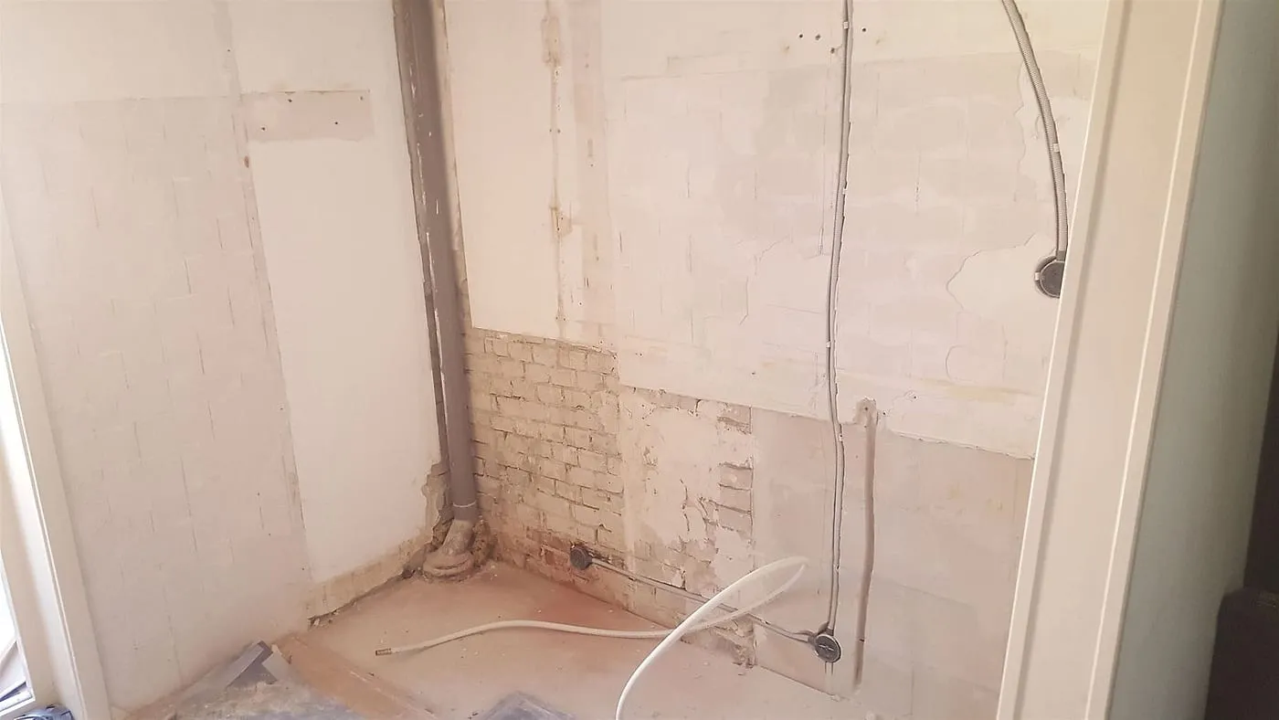 Gestripte keukenwand met oude leidingen vóór de renovatie — keukenrenovatie in Helpman door BontBouw
