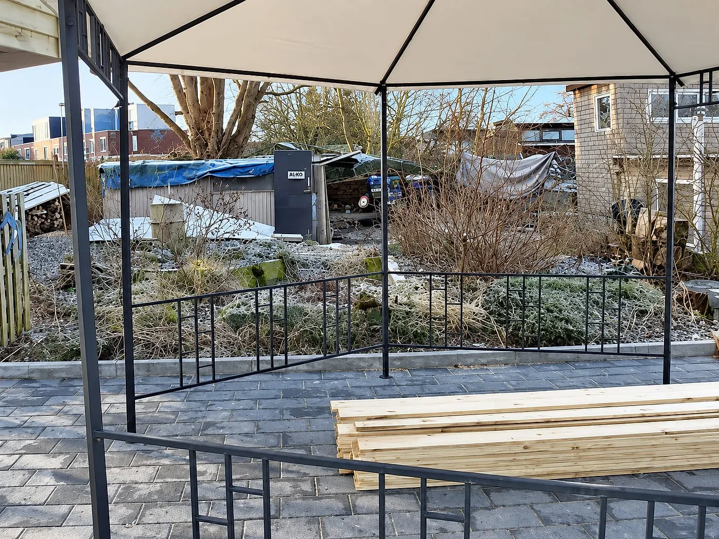 Open tuin met oude schuur en stapel planken bij paviljoen vóór het werk — plaatsen & aanleggen in Groningen door Bontbouw