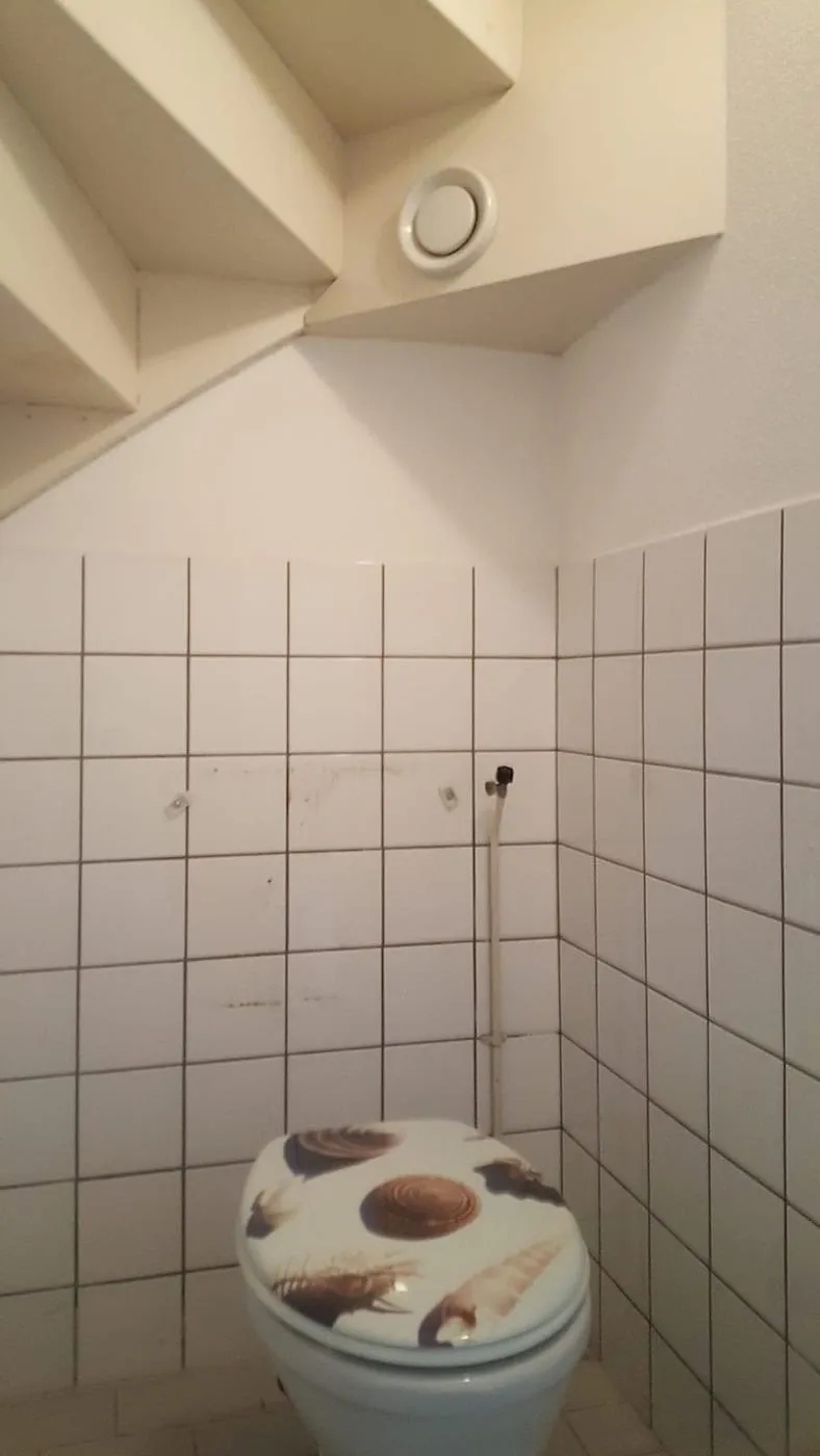 Oud toilet onder de trap met witte tegeltjes vóór de renovatie — toiletrenovatie in De Hunze door BontBouw