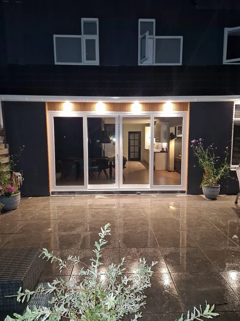 Verlichte schuifpui aan de achtergevel in de avond — complete verbouwing in Beijum door BontBouw