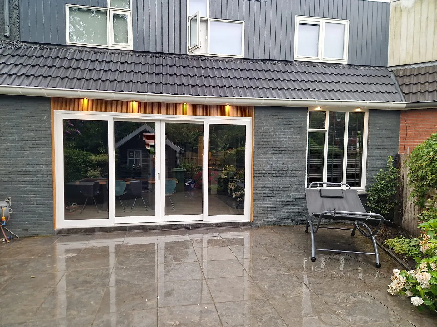 Brede schuifpui in de donkergrijze achtergevel met nieuw terras na de verbouwing — complete verbouwing in Beijum door BontBouw