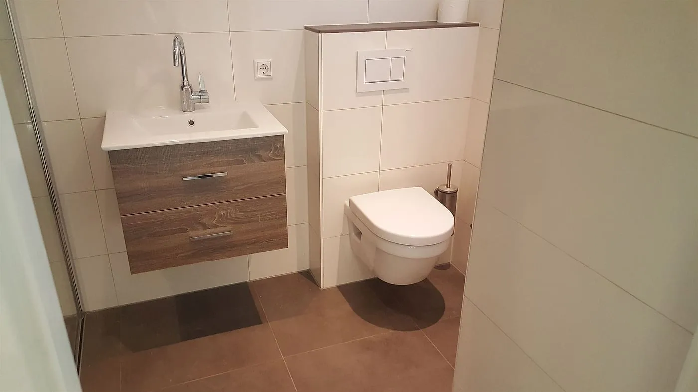 Hangtoilet met inbouwreservoir naast het wastafelmeubel na de renovatie — badkamerrenovatie in Peize door BontBouw