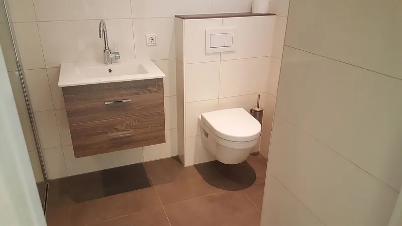 Hangtoilet met inbouwreservoir naast het houten wastafelmeubel — badkamerrenovatie in Peize door Bontbouw