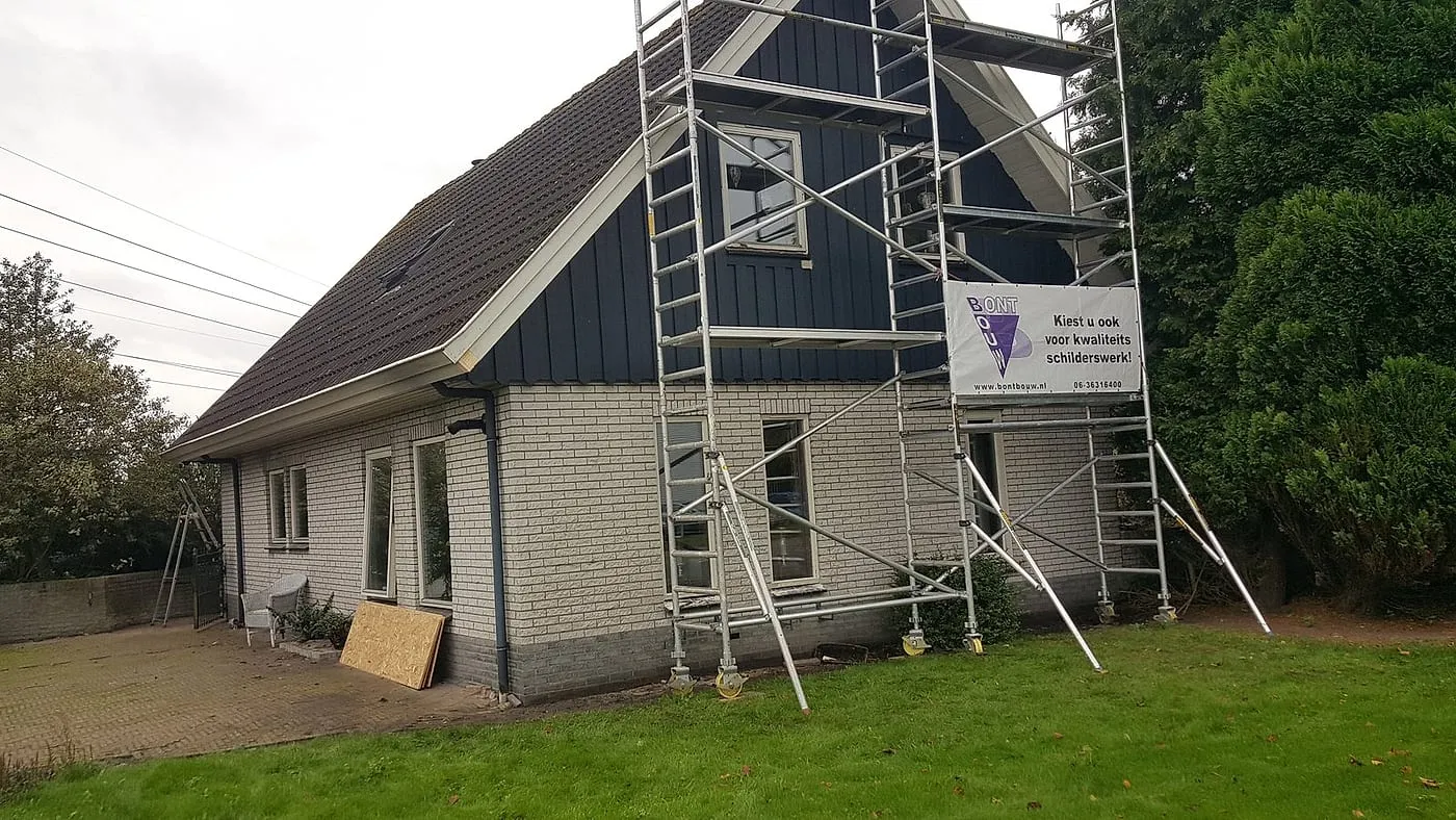 Steiger tegen de blauwe houten topgevel van de woning vóór het werk — schilderwerk in Euvelgunne door BontBouw