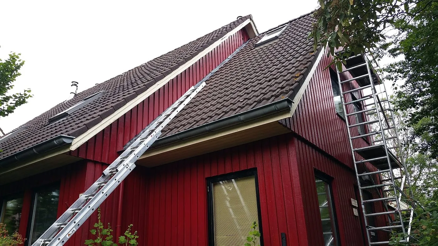 Verweerde dakrand en boeiboord met ladder tegen de gevel vóór het werk — schilderwerk in Beijum door BontBouw
