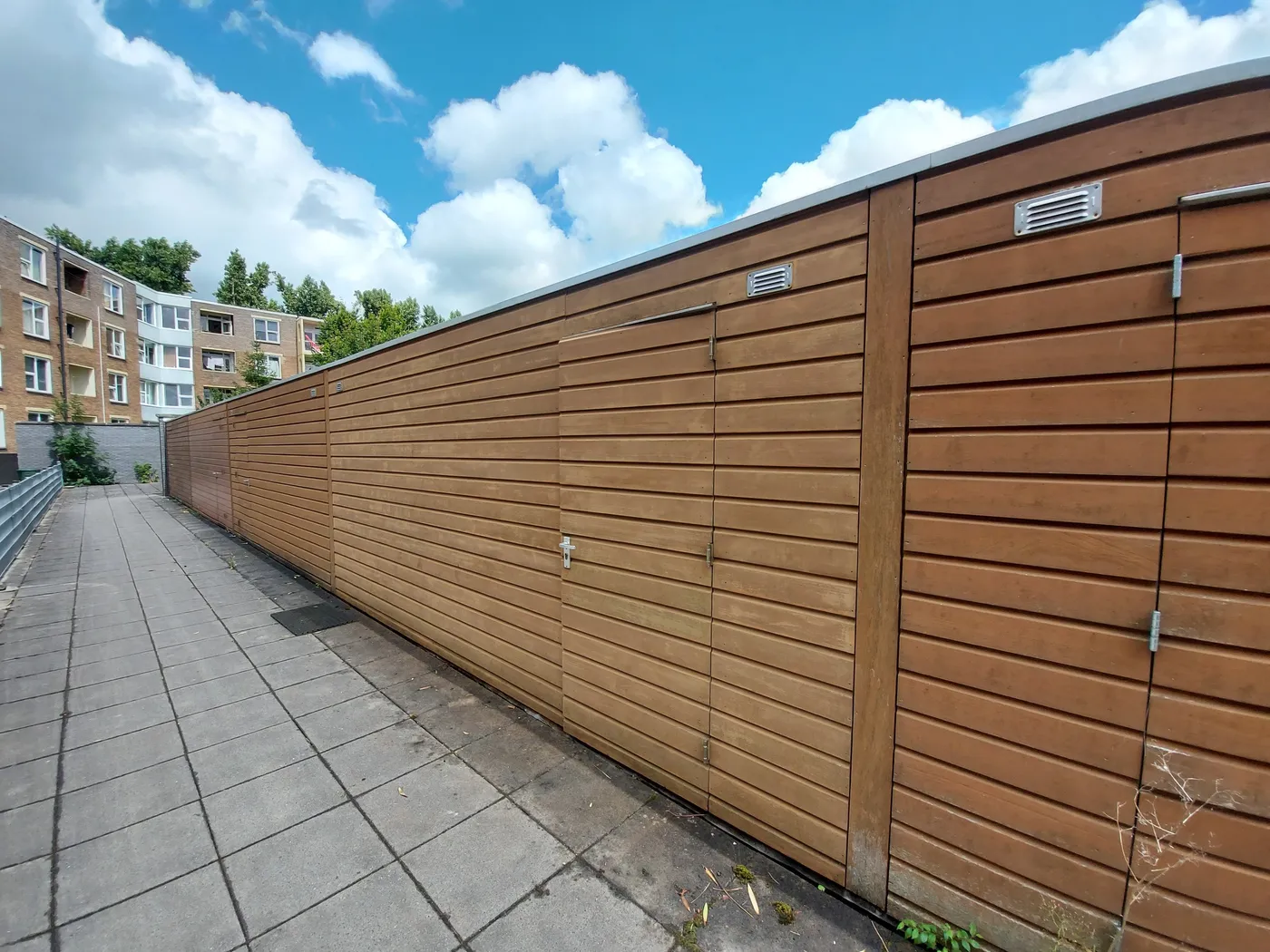 Verweerde houten bergingen langs betegeld pad vóór het werk — schilderwerk in Groningen door BontBouw
