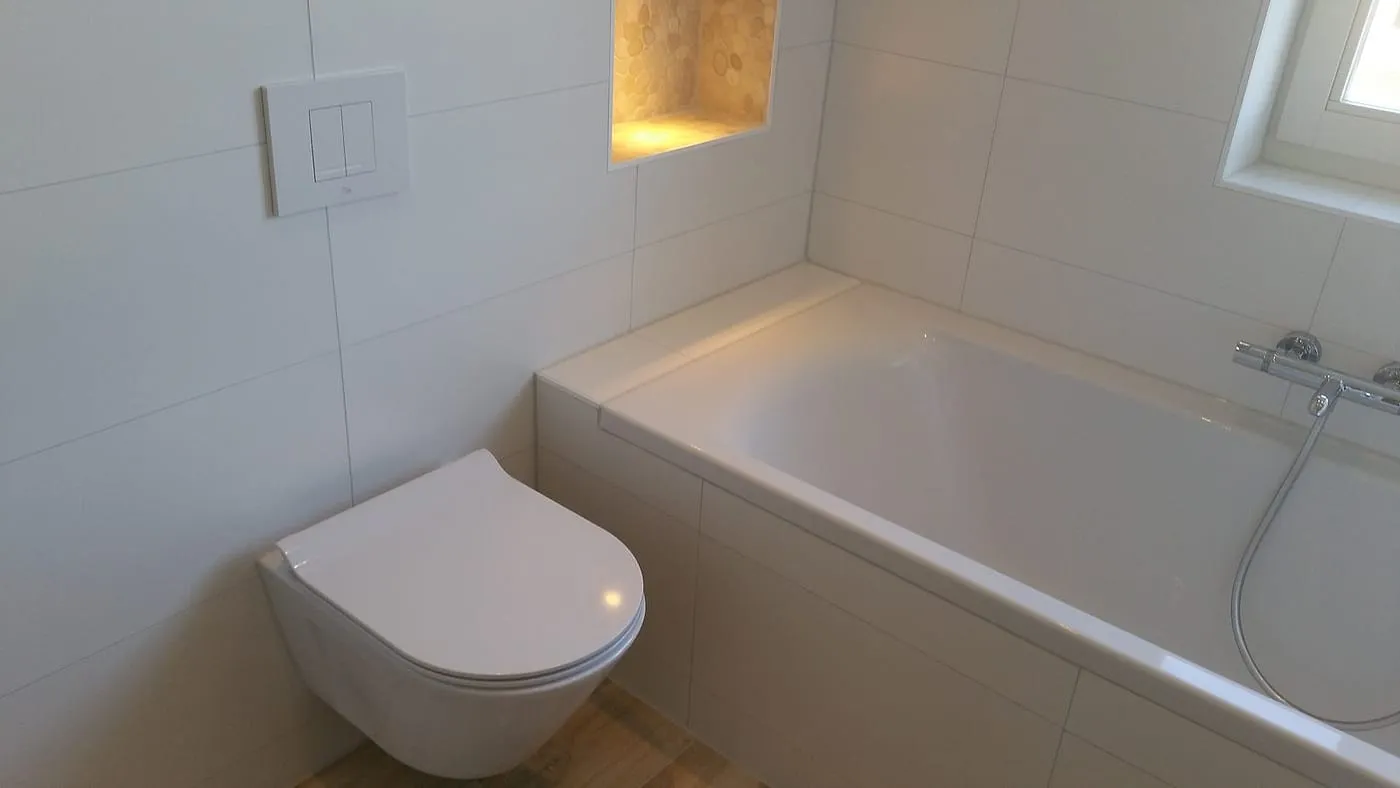 Betegeld ligbad met verlichte kiezelnis en hangtoilet na de renovatie — badkamerrenovatie in Haren door BontBouw