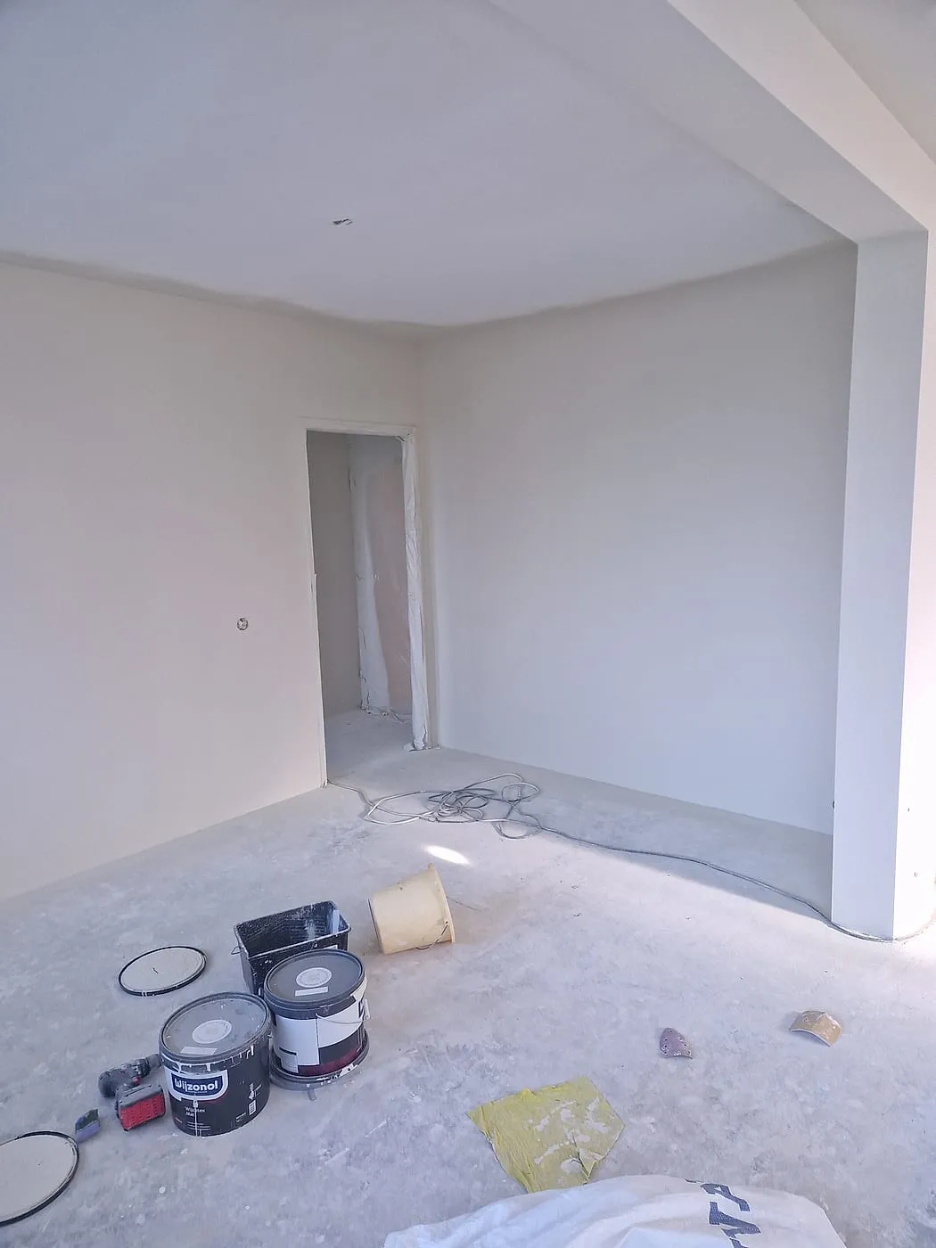 Gestucte kamer met kale betonvloer en verfblikken vóór de verbouwing — complete verbouwing in Apeldoorn door BontBouw