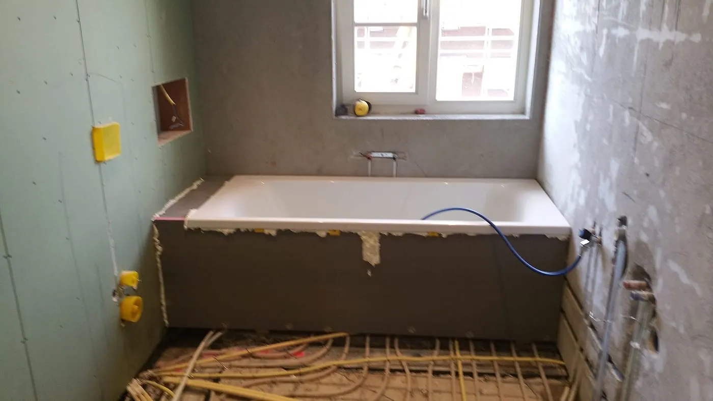 Ingebouwd ligbad tegen onafgewerkte wanden met leidingwerk vóór de renovatie — badkamerrenovatie in Haren door BontBouw