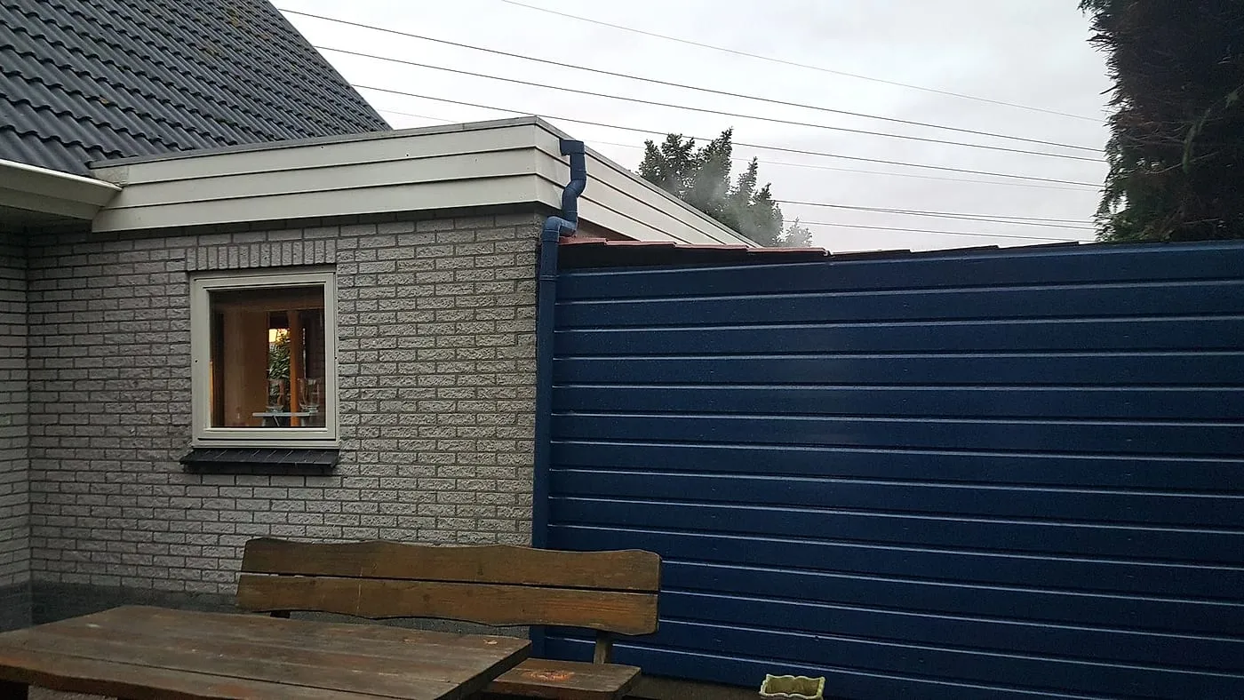 Geschilderde blauwe schuurwand met nieuwe regenpijp en dakrand na het werk — schilderwerk in Euvelgunne door BontBouw