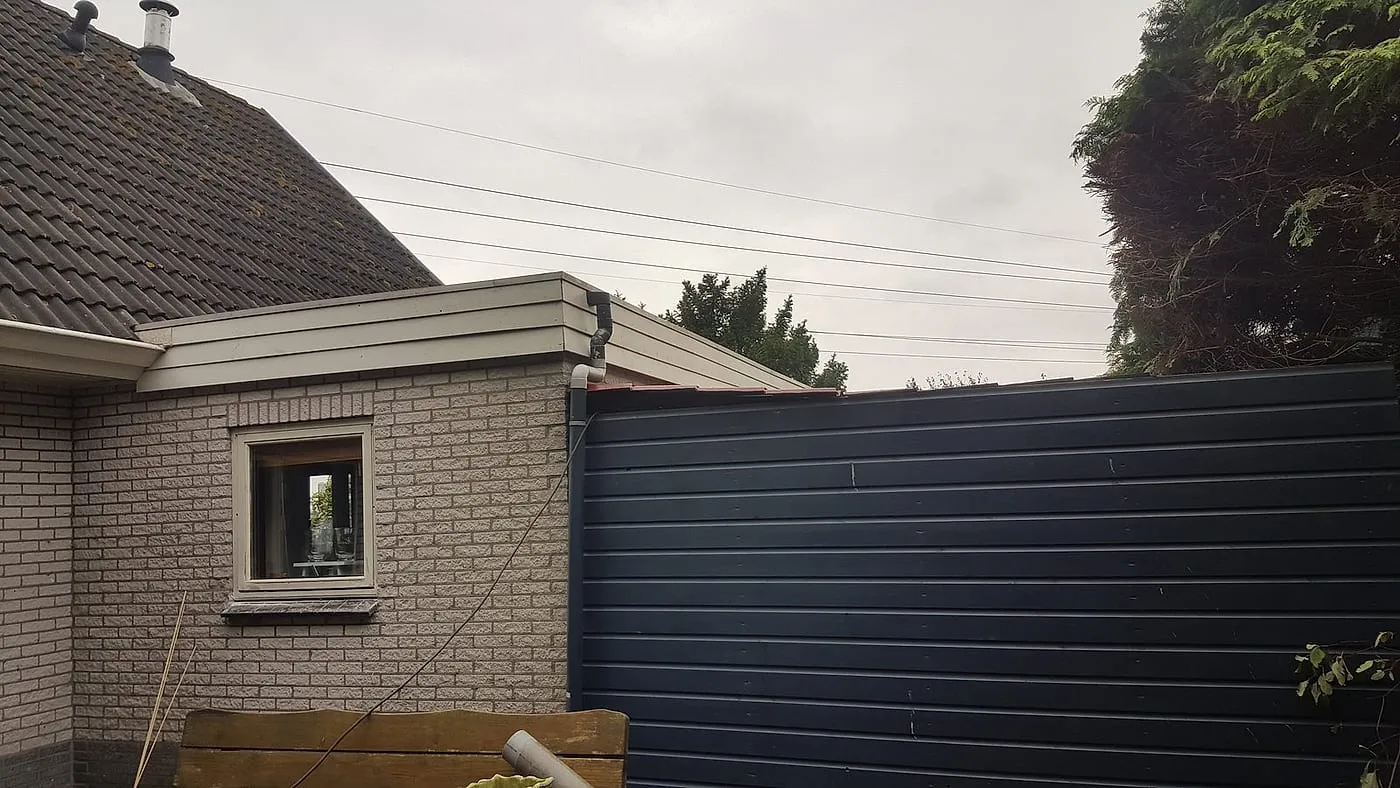 Verweerde donkerblauwe houten schuurwand en dakrand vóór het werk — schilderwerk in Euvelgunne door BontBouw