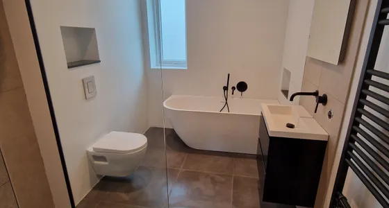 Badkamer met vrijstaand bad, inloopdouche en zwarte handdoekradiator