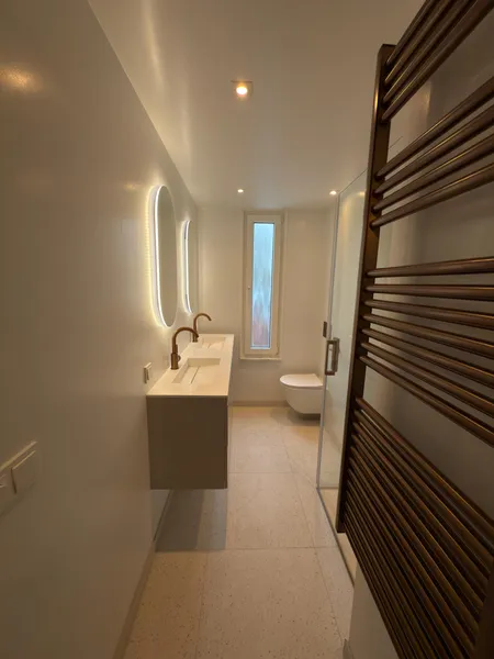 Smalle badkamer met verlichte spiegel en een donkere handdoekradiator